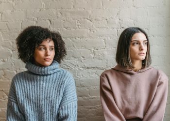 Sad African American woman with female friend in casual clothes looking away while sitting in light room during quarrel at home
