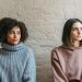 Sad African American woman with female friend in casual clothes looking away while sitting in light room during quarrel at home