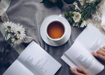 White Ceramic Teacup With Saucer Near Two Books Above Gray Floral Textile