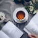 White Ceramic Teacup With Saucer Near Two Books Above Gray Floral Textile